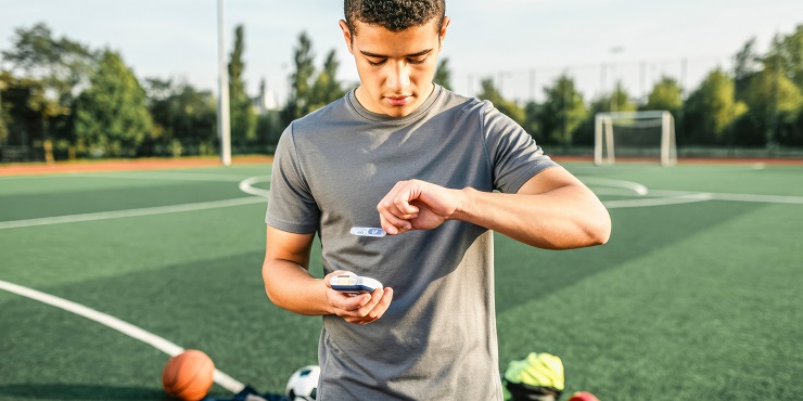 Symbolbild, junger Fußball-Profi misst seinen Blutzucker am Rande des Spielfelds