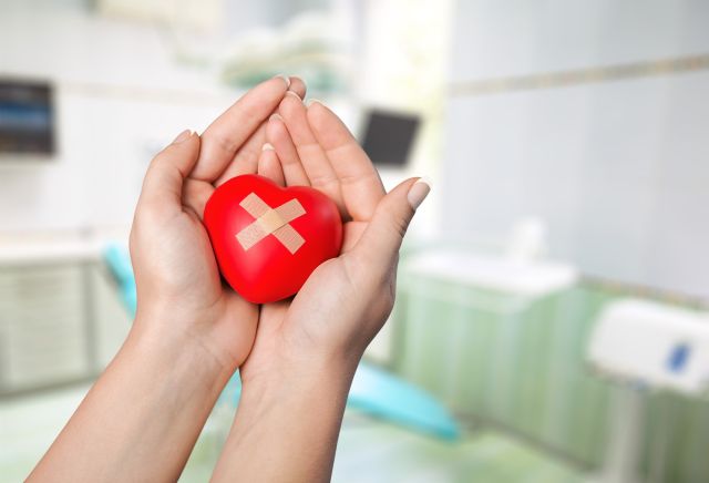 Ein Herz mit zwei Pflastern überkreuz wird in der Mitte von zwei Händen gehalten