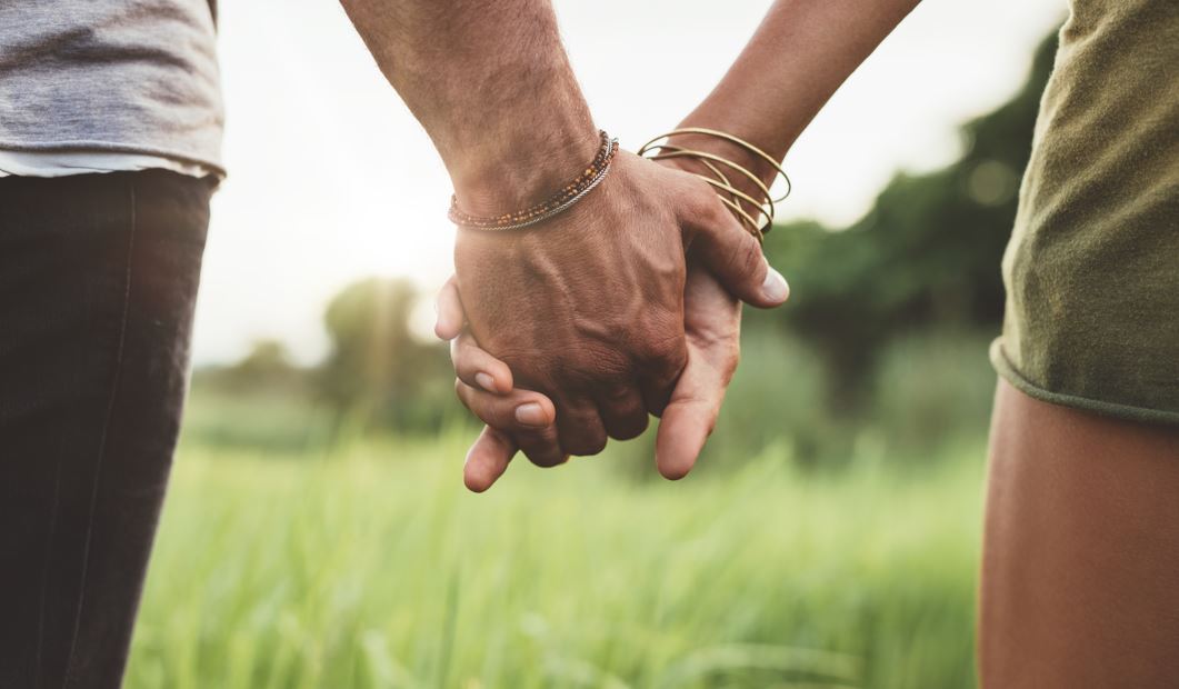 Ein händchenhaltendes Paar vor einer grünen Wiese.