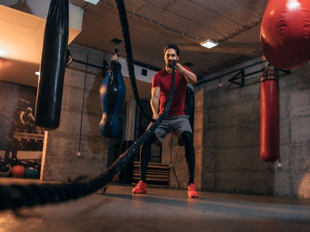 Aufnahme eines fitten jungen Mannes, der im Fitnessstudio mit Kampfseilen trainiert