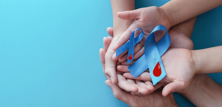 Symbolbild, Hände eines Kindes und eines Erwachsenen halten zwei blaue Schleifen mit einem Bluttropfen