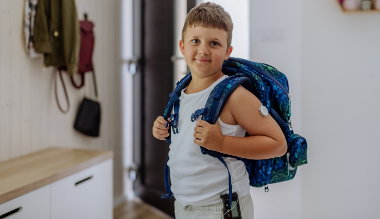Symbolbild, Junge mit CGM und Insulinpumpe geht mit Schulrucksack aus dem Haus