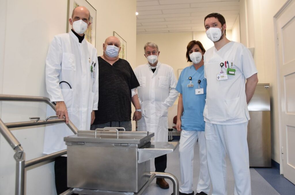 Lutetium-177-PSMA-Therapie: Prof. Dr. Bernd Krause (v. l.), Patient Alexander Huck, Prof. Dr. Oliver Hakenberg, Pflegekraft Dana Senechal und Dr. Martin Heuschkel von der Klinik für Nuklearmedizin mit dem Therapiewagen, der das Medikament enthält. (Foto © Unimedizin Rostock)