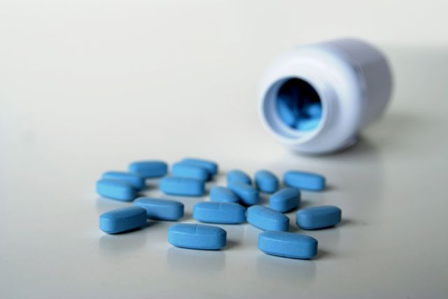 Das Foto zeigt im Hintergrund eine liegende Pillendose, im Vordergrund sind blaue Tabletten als Symbolbild für Sildenafil, das in Viagra enthalten ist, zu sehen.