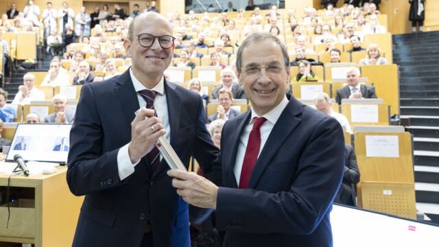 Zwei lachende Männer mit Staffelstab in einem Hörsaal