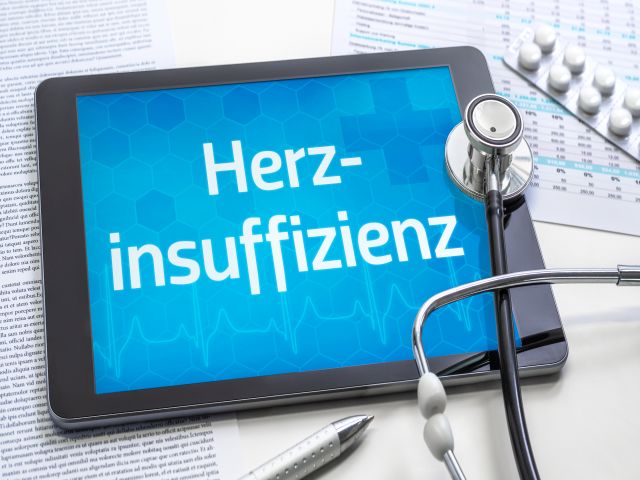 Tablet mit der Aufschrift 'Herzinsuffizienz', umgeben von Stethoskop, Medikamenten und Dokumenten
