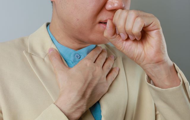 Person zeigt auf den Hals und deutet auf mögliche Hals- oder Kehlkopfprobleme hin.