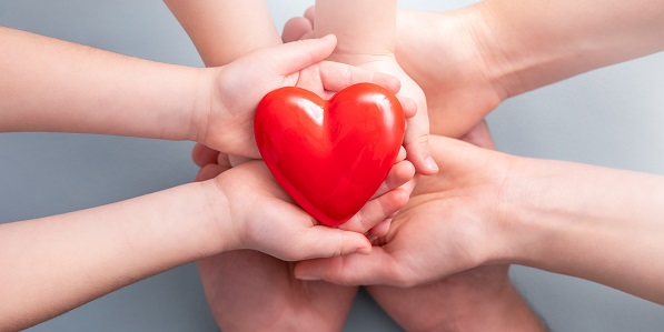 Ein Erwachsener und ein Kind halten ein rotes symbolisches Herz in Händen
