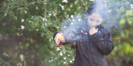 Kleines Mädchen hält einen Feuerwerkskörper, der brennt und raucht.