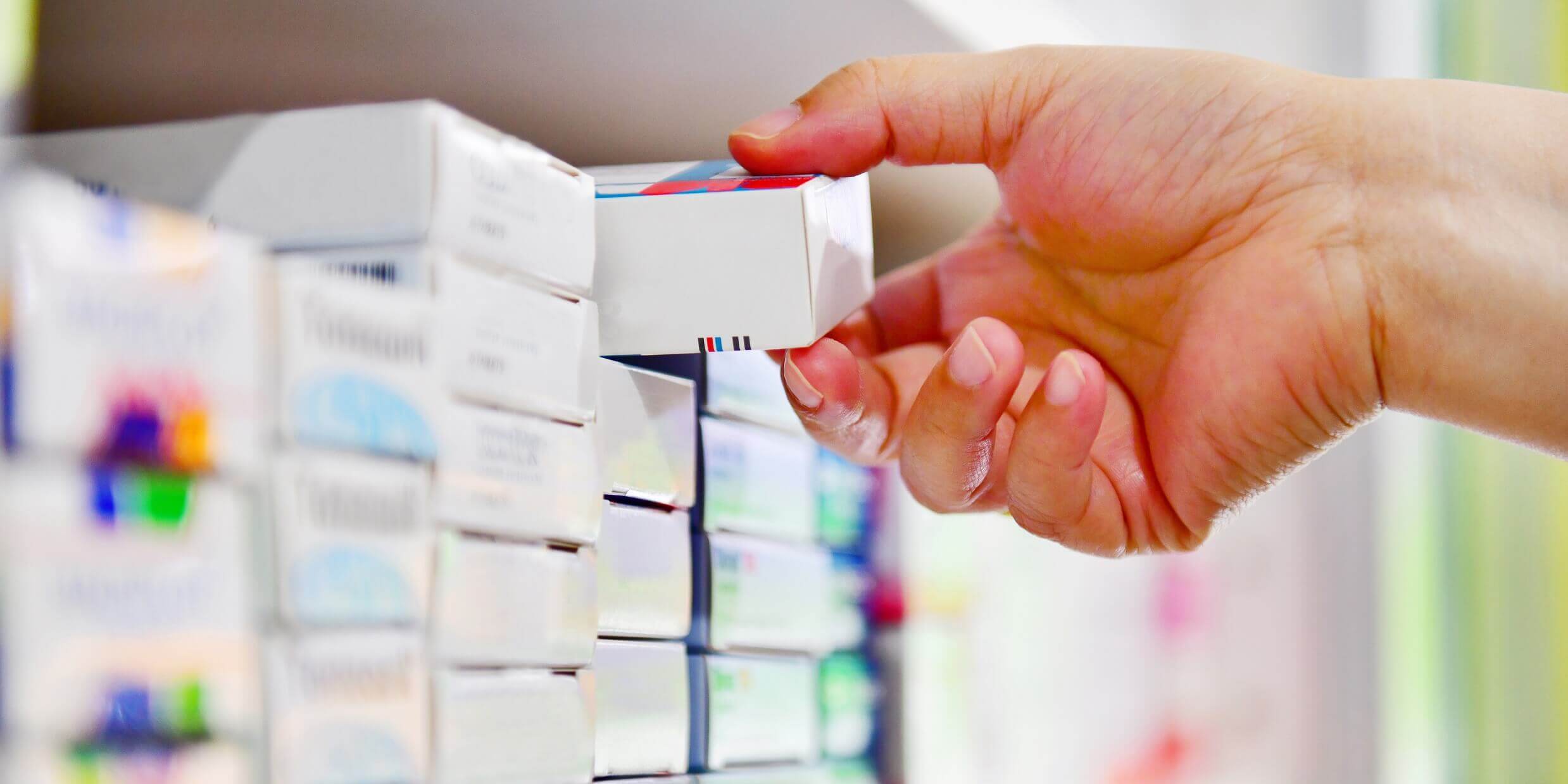 Jemand nimmt eine Packung Arzneimittel aus dem Regal einer Apotheke
