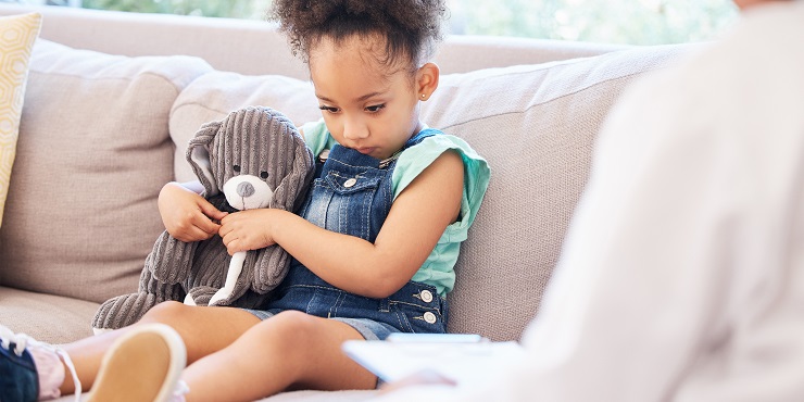 Schweigendes kleines Mädchen sitzt mit Teddy in Arztpraxis