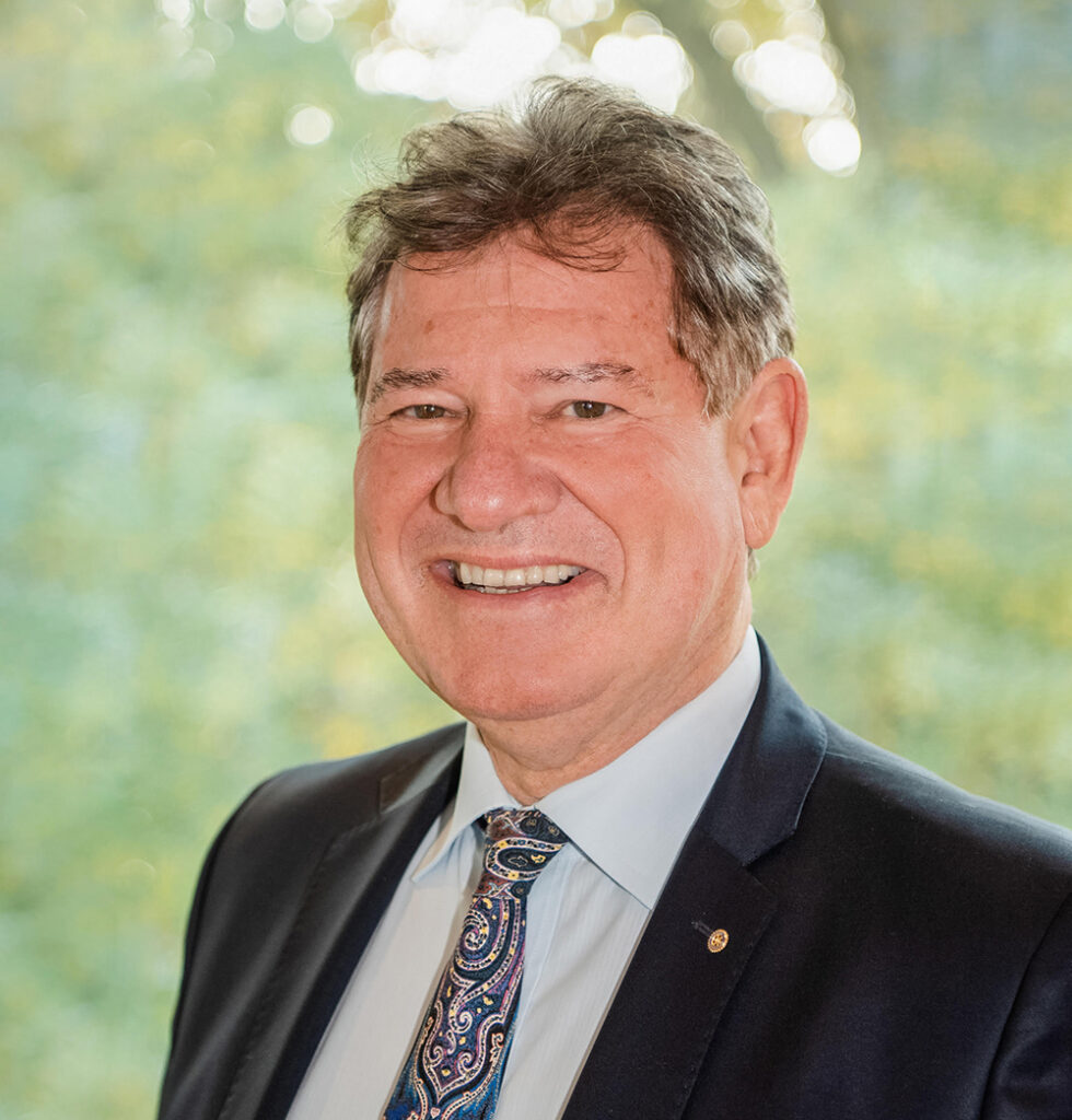 Ein Geschäftsmann im Anzug vor einem unscharfen Naturhintergrund.