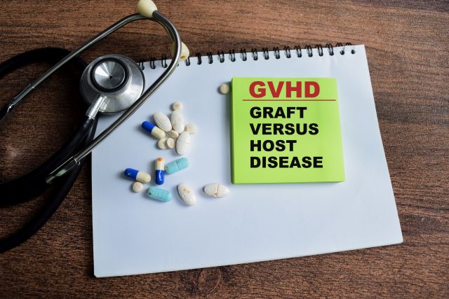 Notizblock mit der Aufschrift ‚GVHD Graft Versus Host Disease‘, umgeben von Medikamenten und einem Stethoskop auf einem Holztisch