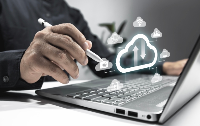 Hand mit Stift zeigt auf ein Laptop mit Cloud-Symbolen, die die Integration und Nutzung von Krebsregisterdaten symbolisieren.