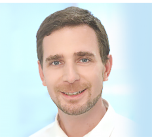 Person mit kurzem braunem Haar trägt ein weißes Hemd vor einem hellblauen Hintergrund.