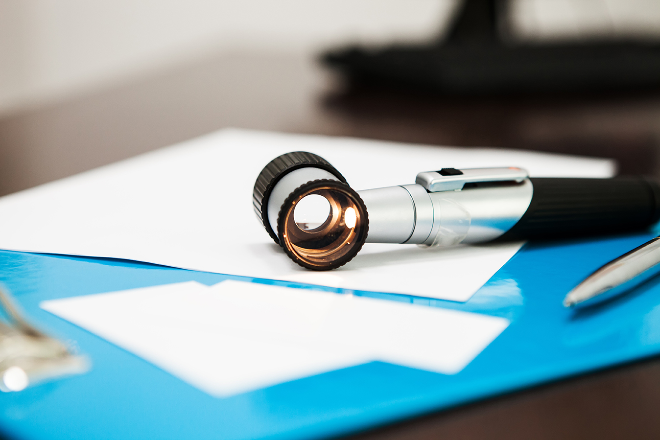 Lupe auf einem Schreibtisch mit Dokumenten und einem blauen Ordner im Hintergrund.