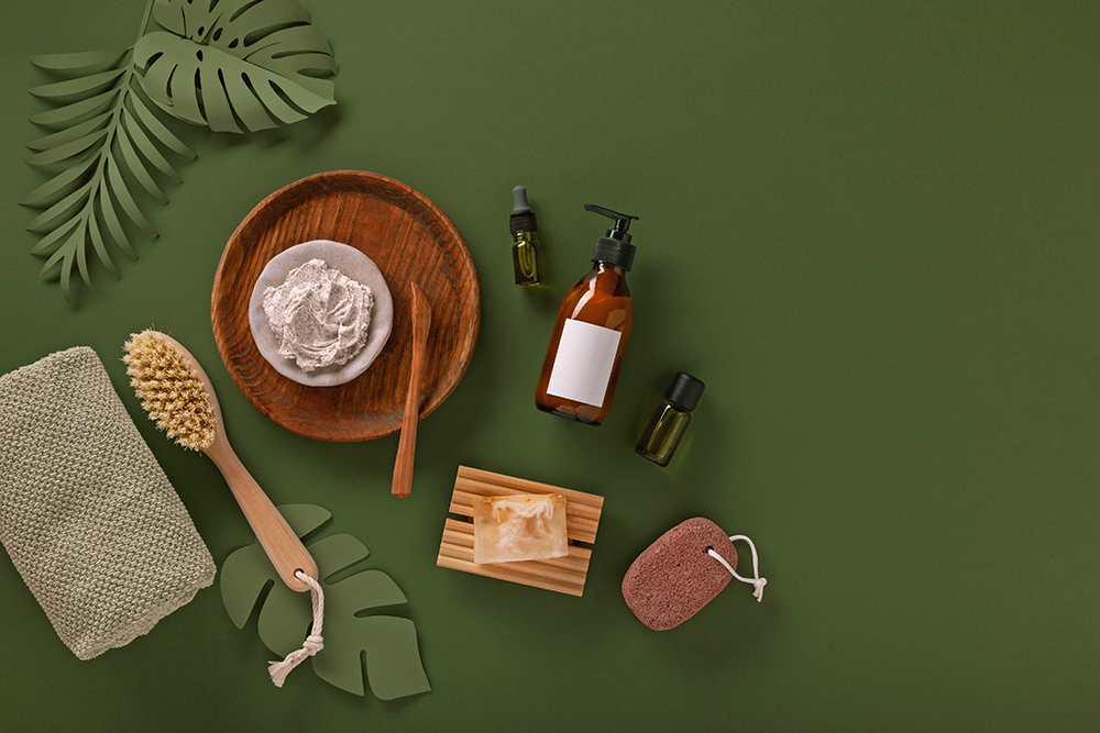 Naturkosmetik-Produkte auf grünem Hintergrund mit Bürste, Seife und Glasflaschen.