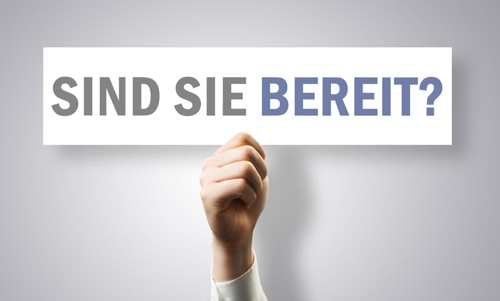 Eine Hand hält ein Schild mit der Aufschrift "Sind Sie bereit?" vor einem grauen Hintergrund.
