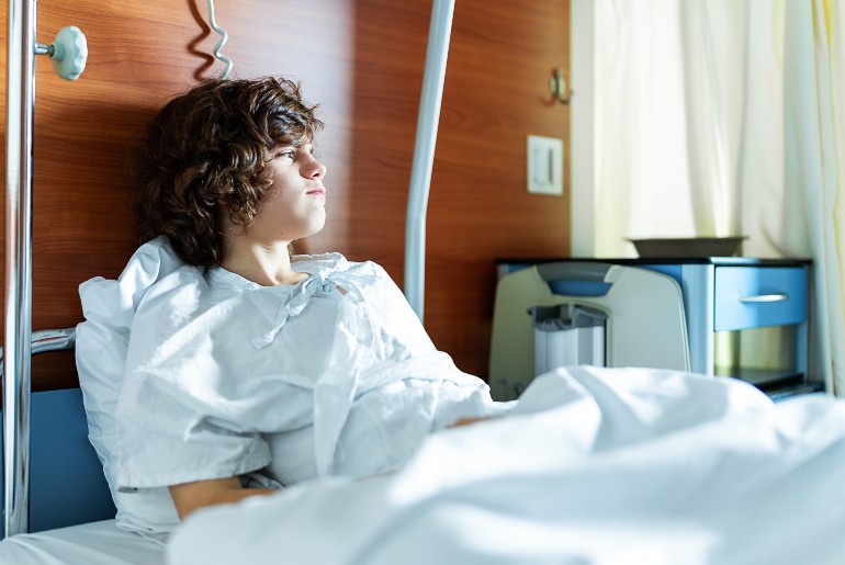 Teenage Junge im Krankenhausbett, trauriger Blick zur Seite.
