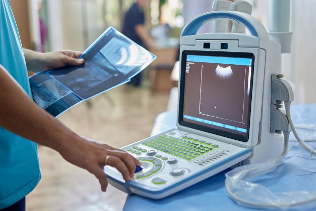 Ultraschallgerät mit Bildschirm und medizinischer Untersuchung im Hintergrund