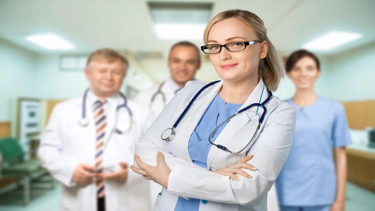 Junge Ärztin im Fokus, hinter ihr stehen zwei Ärzte und eine Ärztin, sie alle lächeln.