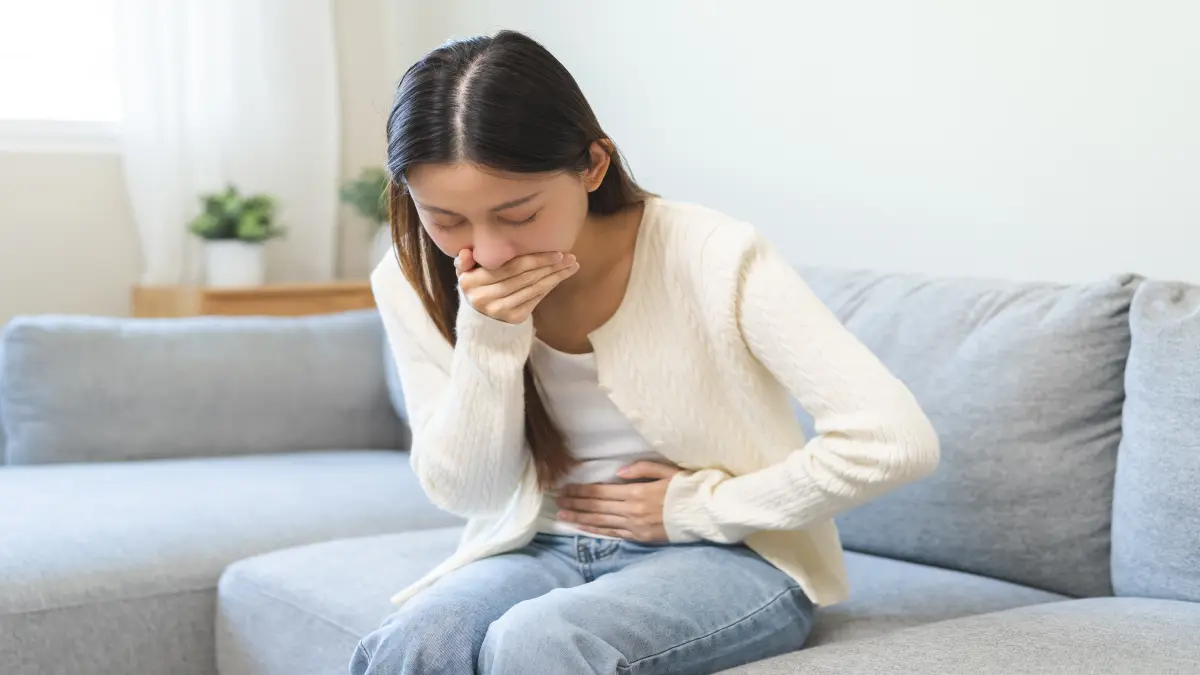 Frau auf Sofa der Übel ist und sich den Bauch hält
