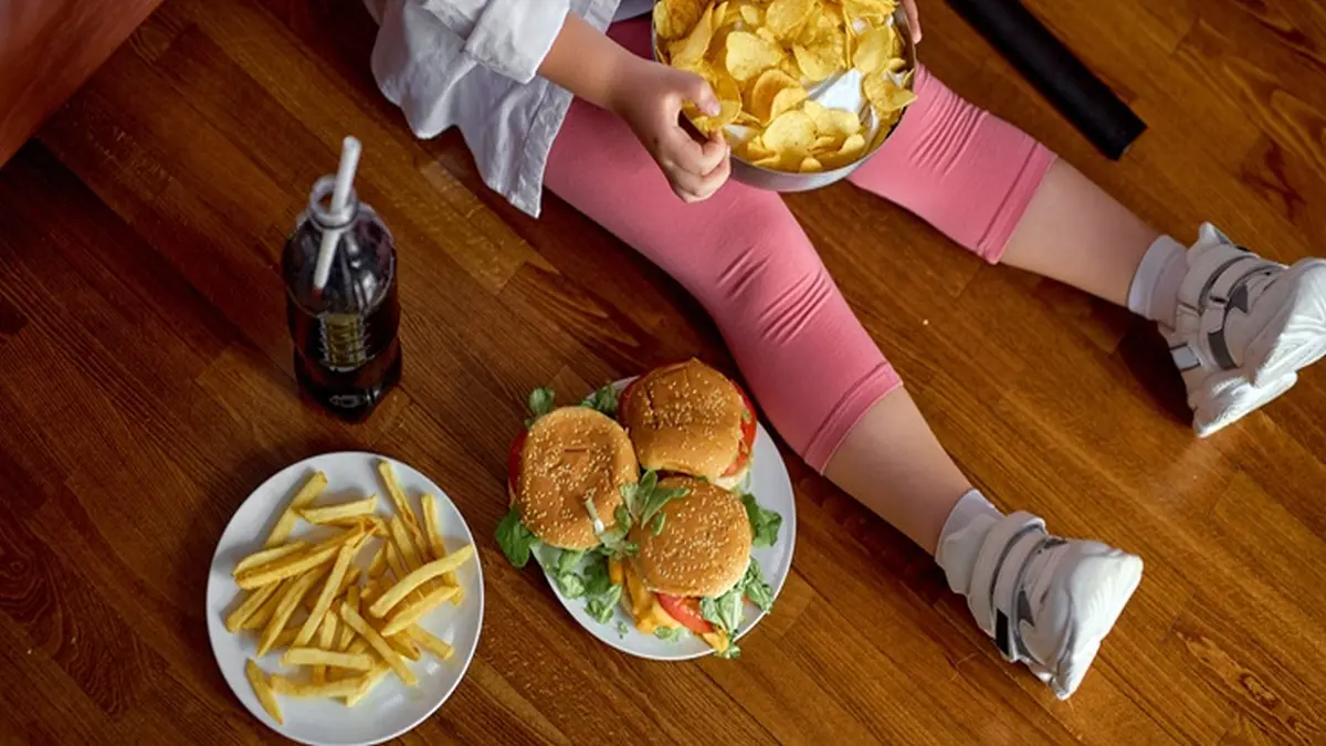Am Boden sitzendes Mädchen mit Chips, Burgern und Pommes Frites