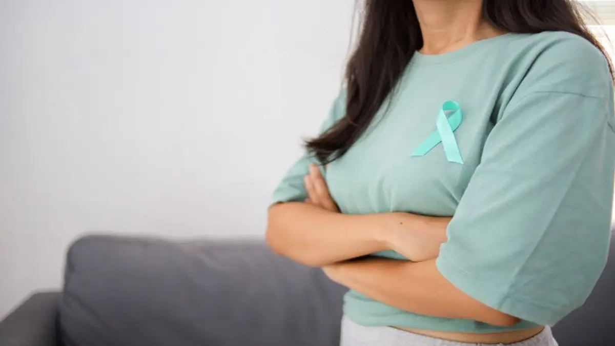 Eine Frau trägt ein tealfarbenes Ribbon auf ihrem T-Shirt – ein Symbol für Brustkrebsaufklärung und Unterstützung.