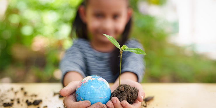 Kind hält kleine Pflanze und Weltkugel in den Händen