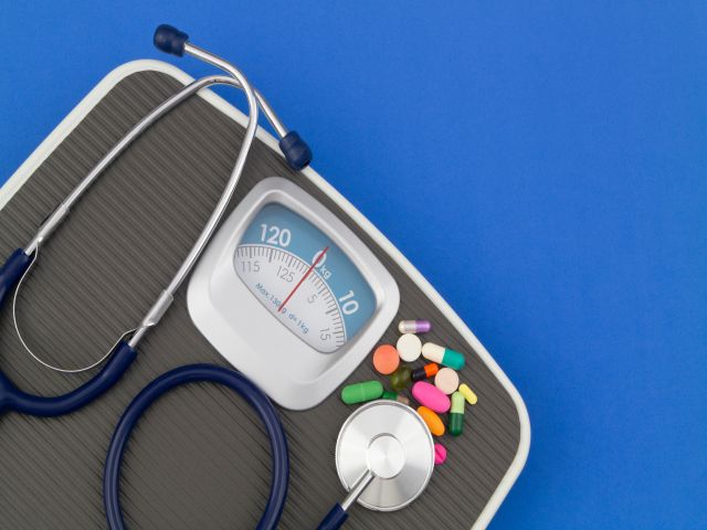 Waage mit Stethoskop und verschiedenen Medikamenten auf blauem Hintergrund.