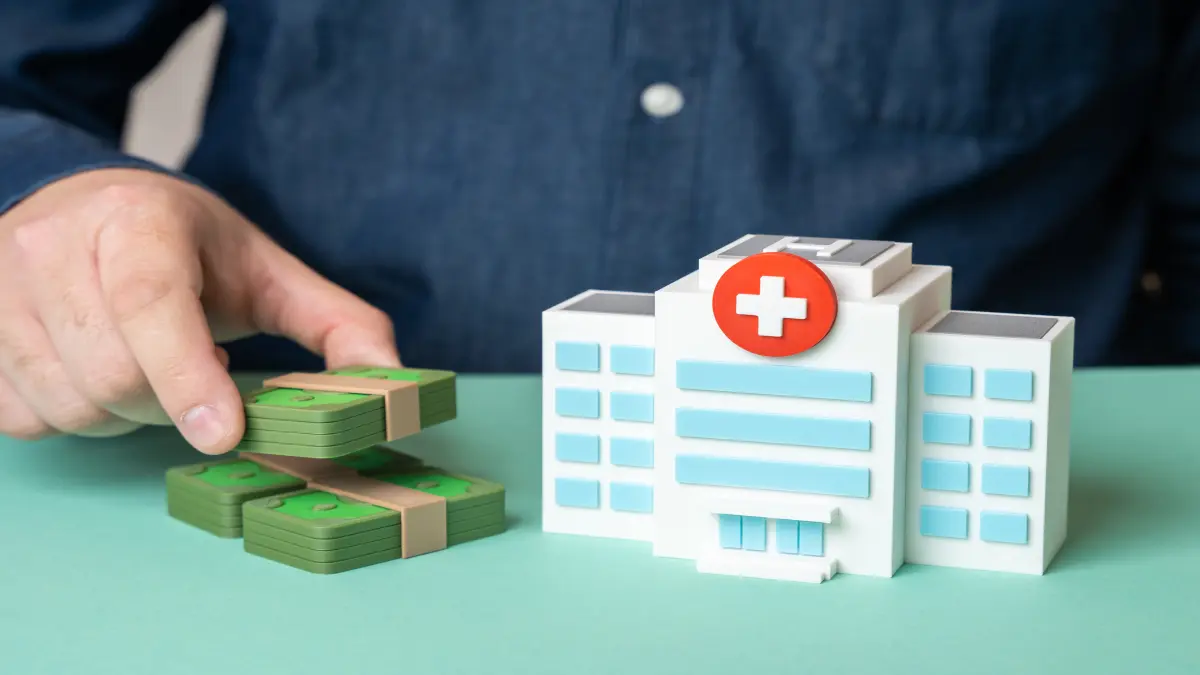 Hand legt Geldscheine neben ein Krankenhausmodell als Symbol für medizinische Förderung