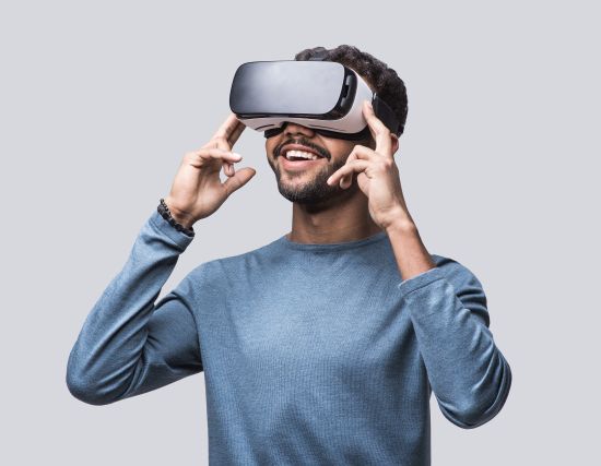 Mann trägt VR-Headset und hebt die Hände an die Seiten des Geräts, grauer Hintergrund.