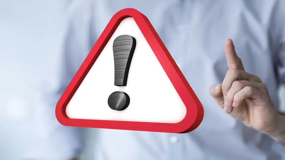 Rotes Warnschild mit Ausrufezeichen vor unscharfem Hintergrund, Person hebt mahnend den Finger