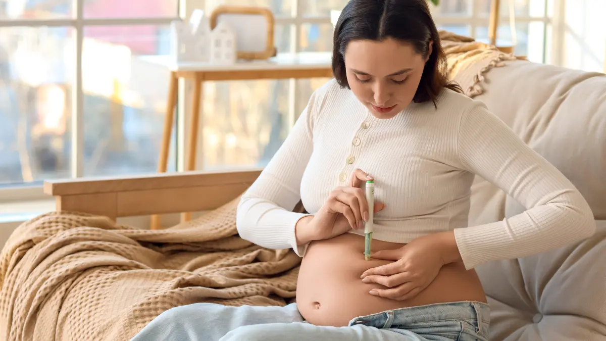 junge schwangere Frau spritzt sich auf dem Sofa sitzend Insulin in den Bauch