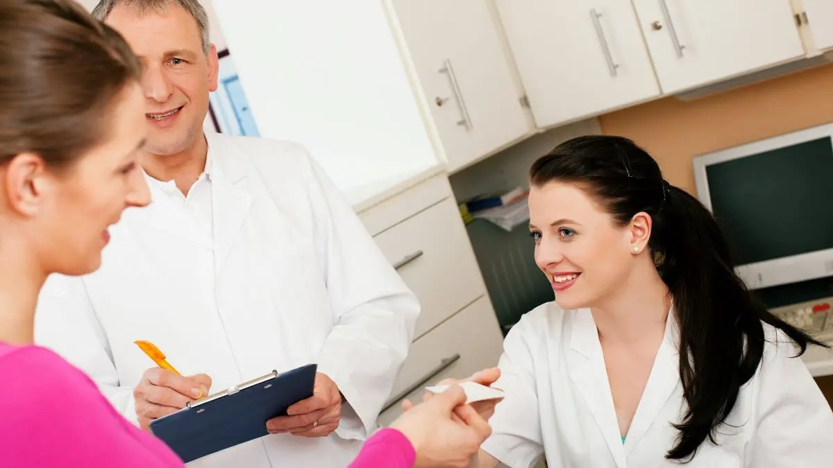 Patientin am Empfang einer Arztpraxis, während medizinisches Personal Informationen austauscht.