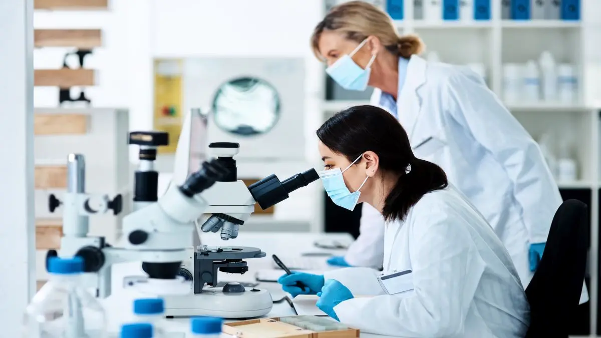 Zwei Wissenschaftlerinnen im Labor arbeiten mit einem Mikroskop, um Gewebeproben für die Brustkrebsdiagnostik zu analysieren.