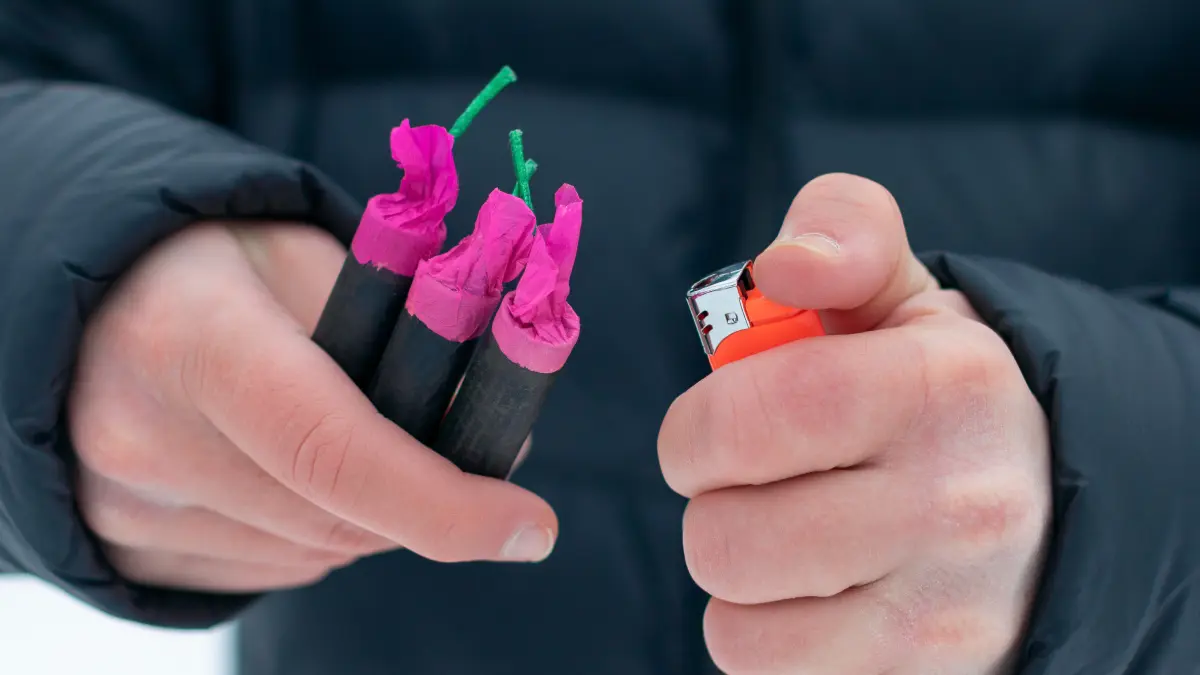 Hände eines Jugendlichen, der Böller und ein Feuerzeug hält