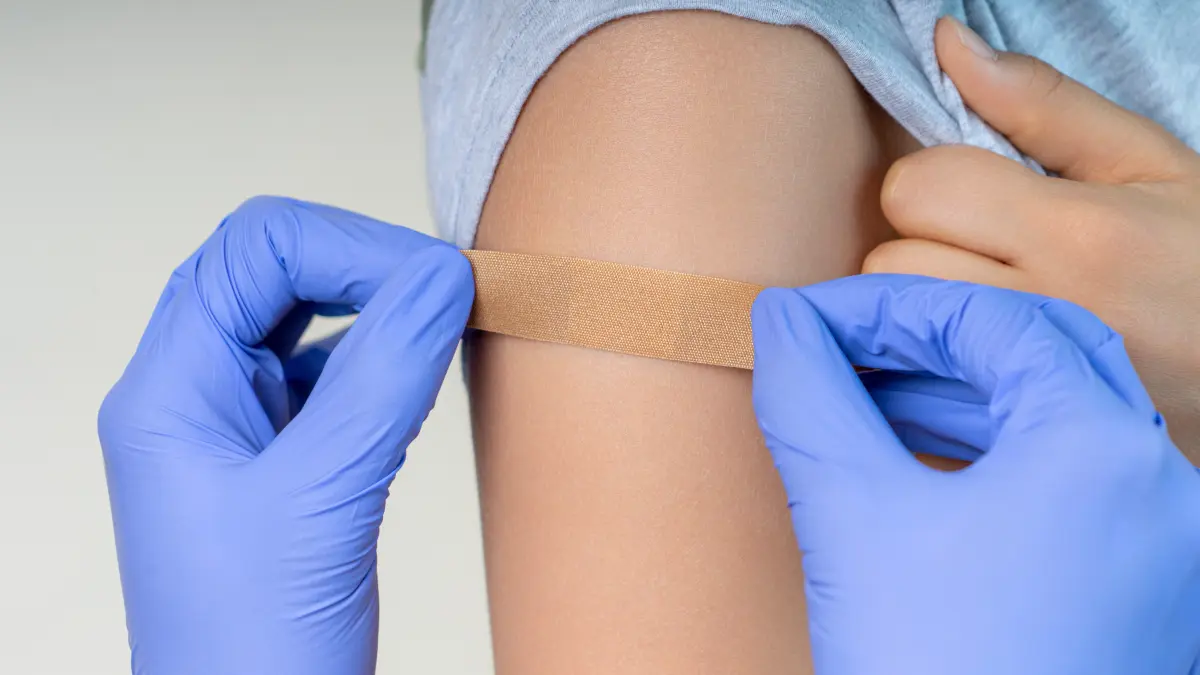 Arzt klebt nach der Impfung Pflaster auf Oberarm eines Jugendlichen.
