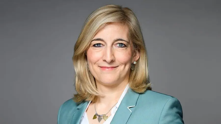 Portrait von Nina Warken in einem türkisfarbenen Blazer vor einem neutralen grauen Hintergrund.