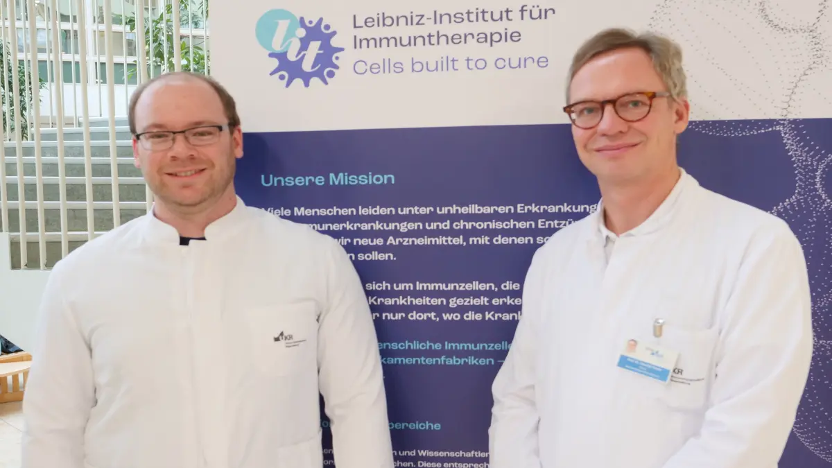 Sascha Göttert und Prof. Hendrik Poeck stehen vor einem Banner des Leibniz-Instituts für Immuntherapie.