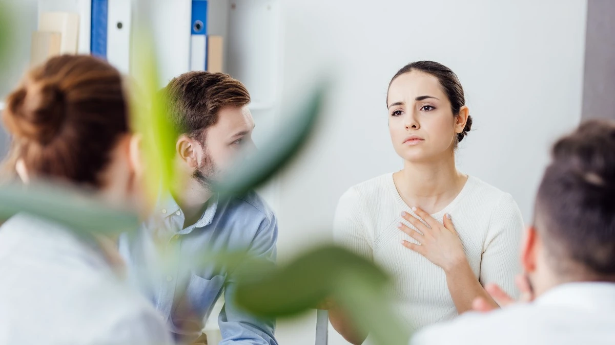 Einblick in eine Gruppentherapie-Stunde. In einem Stuhlkreis sitzen sich vier Erwachsene gegenüber. Eine Frau gestikuliert.