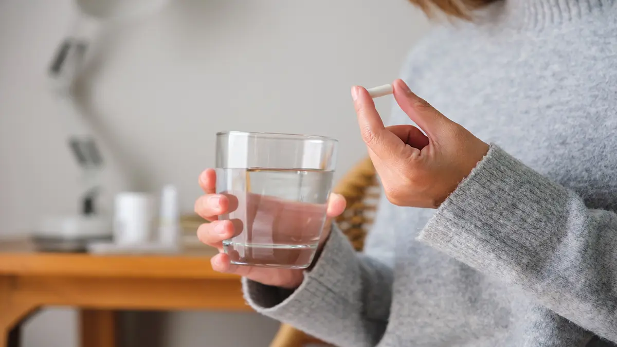 Person hält ein Glas Wasser und eine Tablette, bereit zur Einnahme.