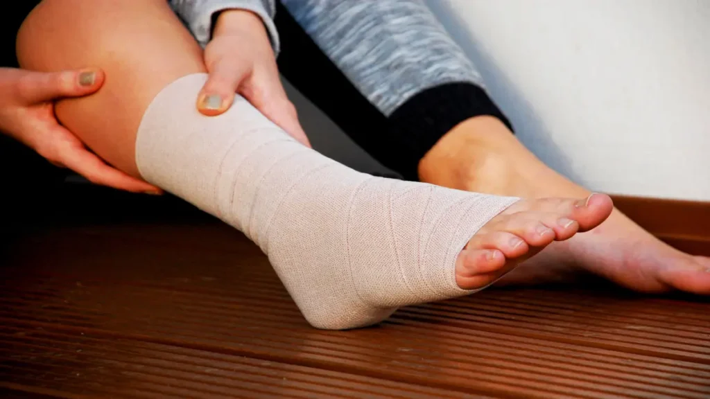 Fuß mit elastischer Bandage, Person hält den Unterschenkel – typischerweise nach einer Verletzung wie Verstauchung oder Zerrung.