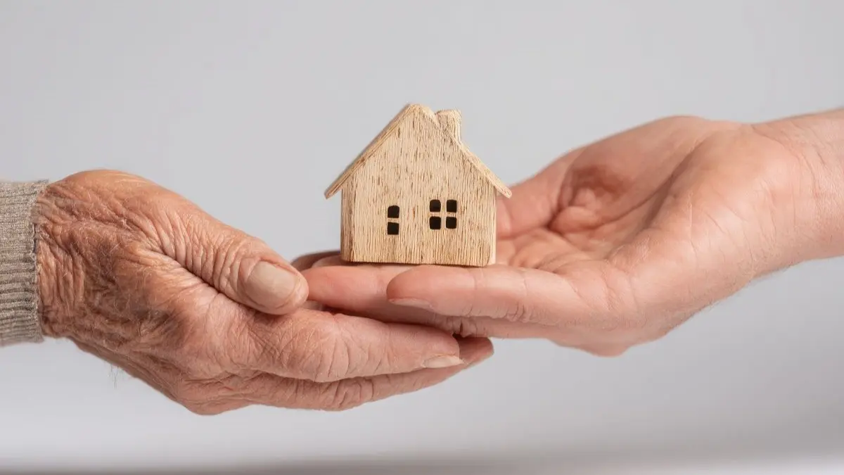 Aeltere und juengere Hand halten gemeinsam Holzhaus-Modell – Symbol fuer Erbschaftsteuer Familienheim und Steuerbefreiung