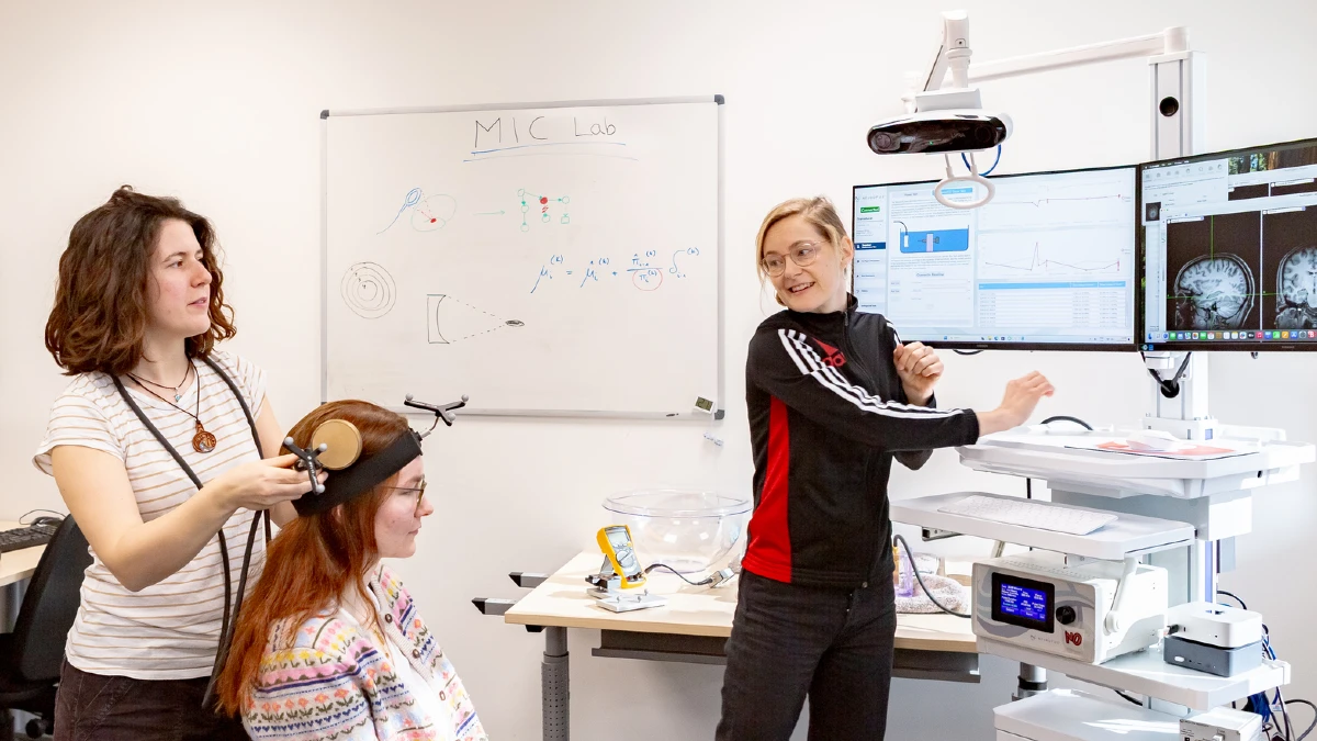 EEG-Messung im MIC Lab: Forscherin legt Probandin Elektroden an, Wissenschaftlerin erklärt Gehirndaten am Monitor