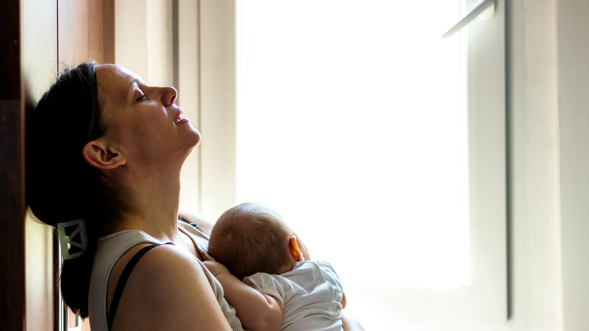 Erschöpfte Mutter hält schlafendes Baby im Arm – postnatale Depression und mütterliche Erschöpfung