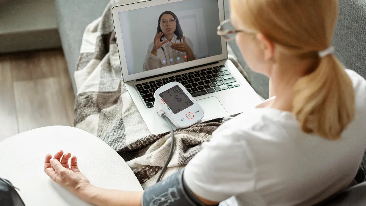 Person misst zu Hause den Blutdruck und spricht per Videosprechstunde mit medizinischem Fachpersonal