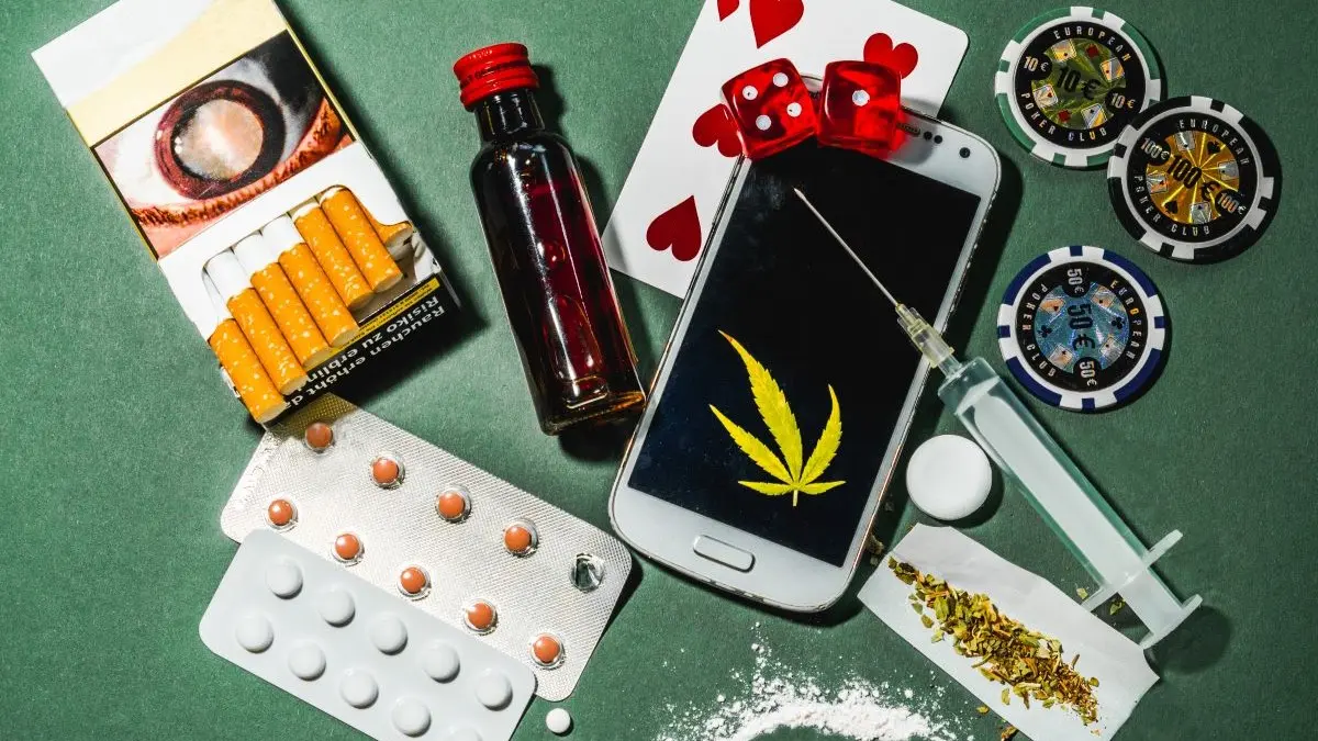 Cigaretten Alkohol Tabletten Spritze Pulver Smartphone mit Cannabisblatt und Spielchips auf einem Tisch, Symbolbild fuer verschiedene Suchterkrankungen bei Acne inversa