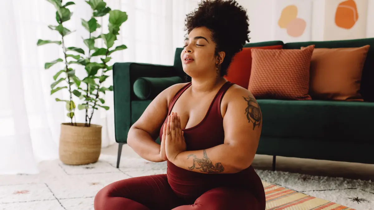 Frau macht Entspannungsuebungen im Wohnzimmer in einer Yoga-Meditationshaltung