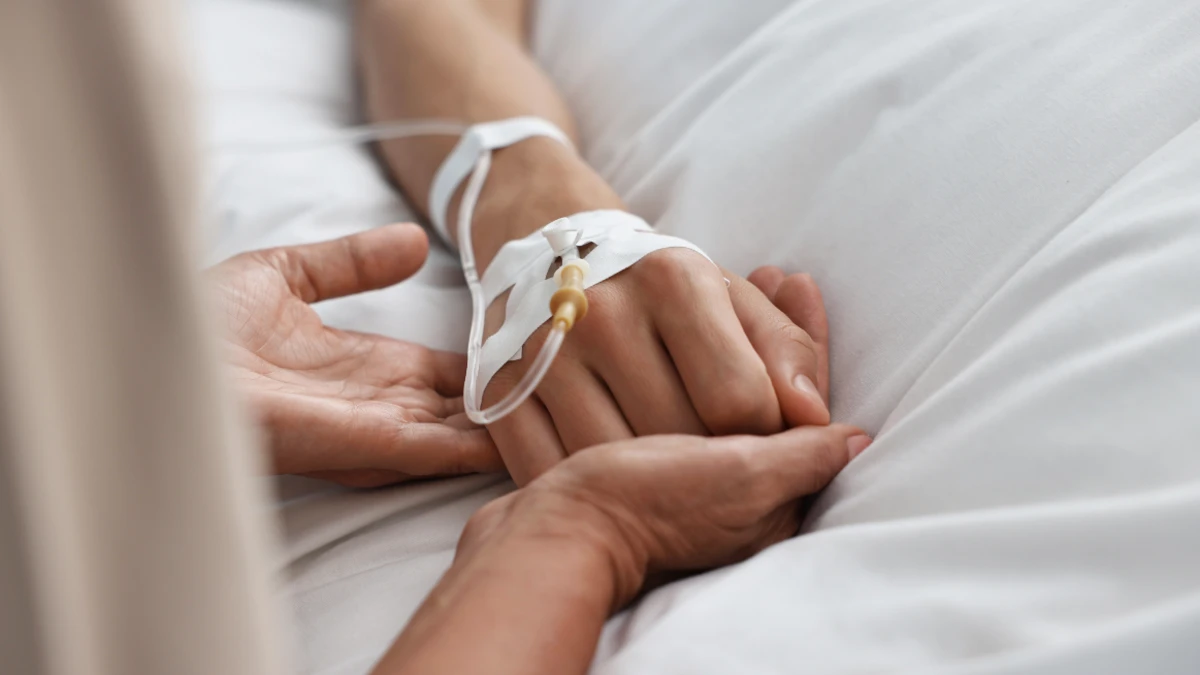 Pflegende Hand hält die Hand eines Patienten mit IV-Zugang auf der Neurointensivstation